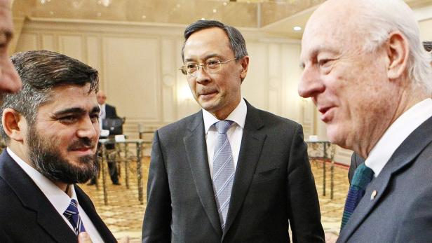 Drei Männer in Anzügen unterhalten sich in einem Raum.