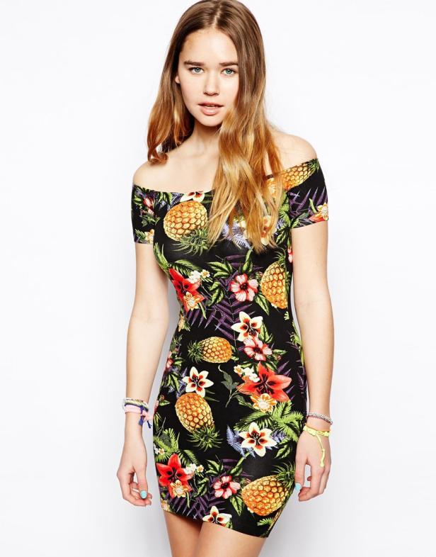 Eine junge Frau trägt ein schulterfreies Kleid mit Ananas- und Blumenmuster.