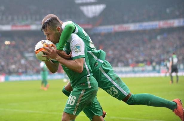 Ein Fußballspieler küsst den Ball, während ein anderer ihn umarmt.