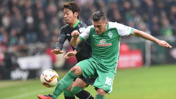 Ein Fußballspieler von Werder Bremen schießt den Ball, während ein Gegenspieler ihn zu stoppen versucht.