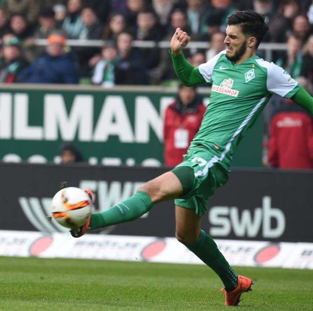 Ein Fußballspieler in Grün schießt einen Ball vor einer Zuschauermenge.
