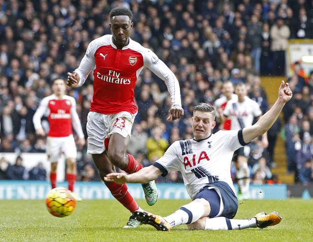Ein Fußballspieler von Arsenal dribbelt den Ball, während ein Spieler von Tottenham zu Boden geht.