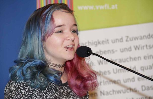 Eine junge Frau mit blau und pink gefärbten Haaren spricht in ein Mikrofon.