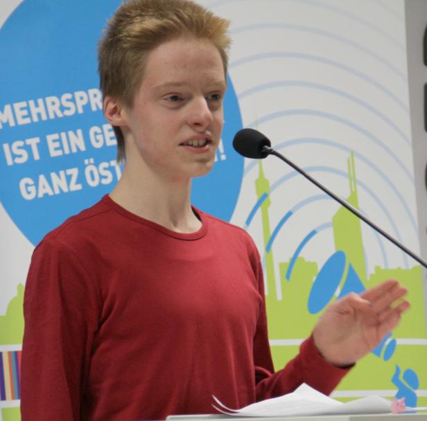 Ein junger Mann spricht bei einer Veranstaltung in ein Mikrofon.