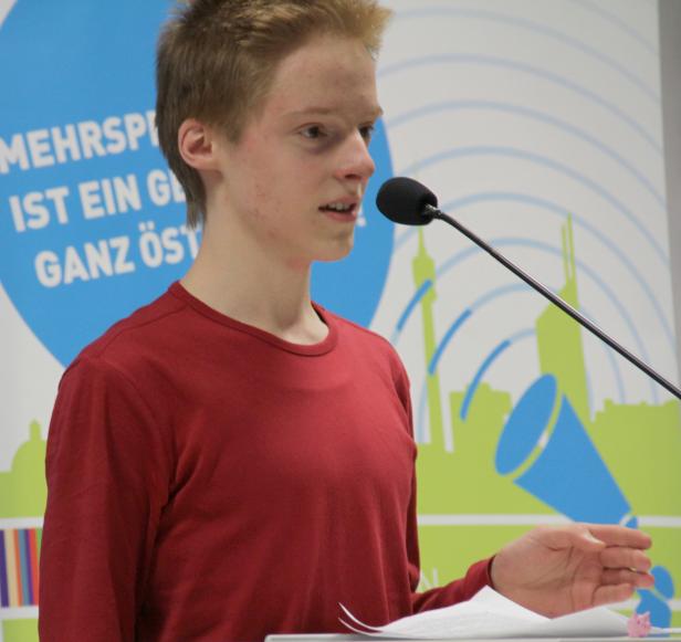 Ein junger Mann spricht bei einer Veranstaltung in ein Mikrofon.