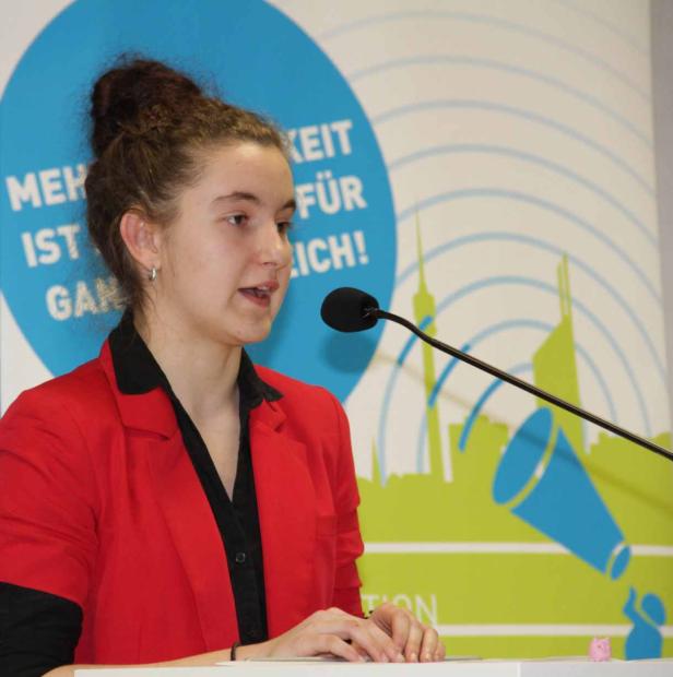 Eine junge Frau hält eine Rede vor einem Mikrofon.