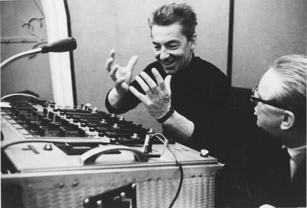 Leonard Bernstein gestikuliert vor einem Mischpult, während ein Mann ihm zusieht.