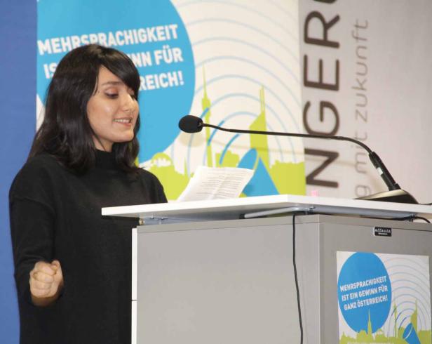 Eine Frau hält eine Rede an einem Rednerpult mit dem Slogan „Mehrsprachigkeit ist ein Gewinn für ganz Österreich!“.