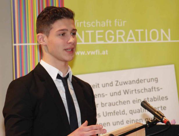 Ein junger Mann hält eine Rede vor einem Banner zum Thema Integration.
