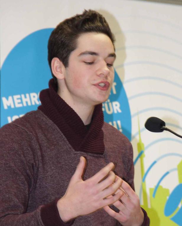 Ein junger Mann spricht vor einem Mikrofon auf einer Veranstaltung.