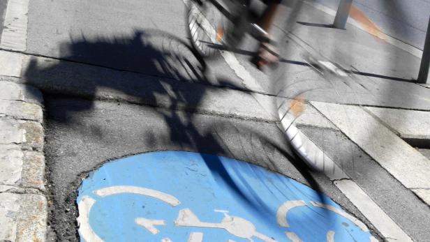 Ein Fahrradfahrer fährt über einen Radweg, dessen blaues Symbol auf dem Asphalt zu sehen ist.