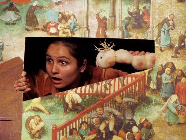 Eine Frau blickt überrascht auf eine Wurstpuppe vor einem Ausschnitt aus einem Gemälde von Pieter Bruegel dem Älteren.