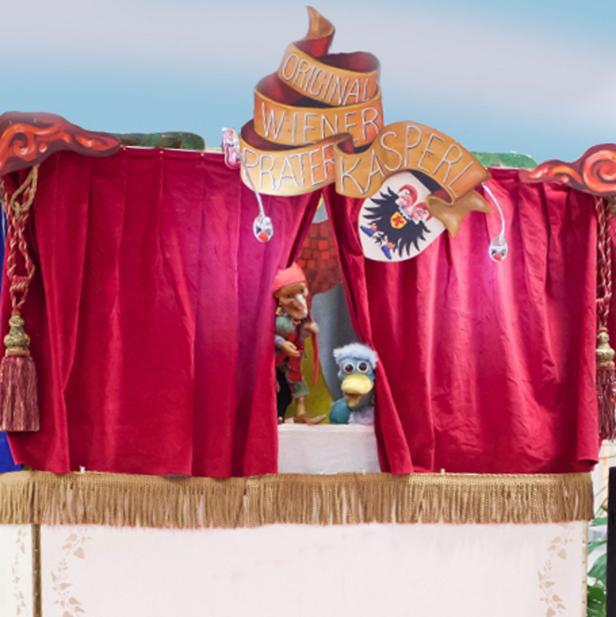 Ein Kasperletheater mit roten Vorhängen und den Puppen Kasperl und einer Ente.