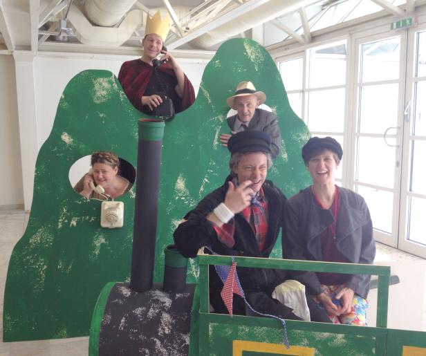 Eine Gruppe von Personen posiert hinter einer bemalten Zugkulisse.