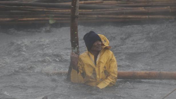 Ein Mann in gelber Regenkleidung steht im Hochwasser und hält sich an einem Pfosten fest.