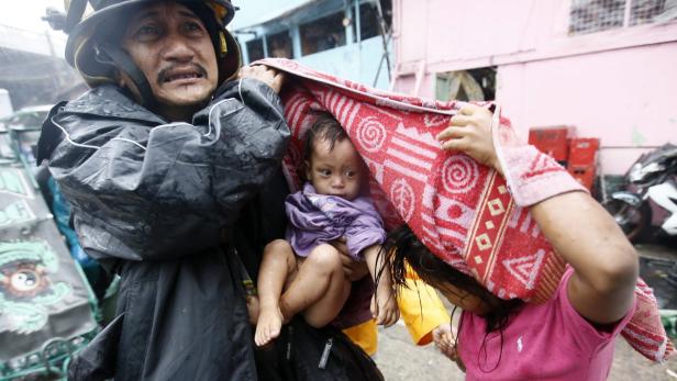 Ein Feuerwehrmann trägt ein Baby, das mit einem Handtuch vor dem Regen geschützt wird.
