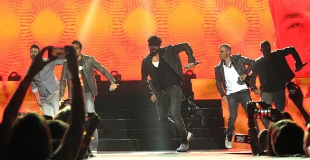 Die Backstreet Boys treten auf einer Bühne vor einem roten Bildschirm auf.