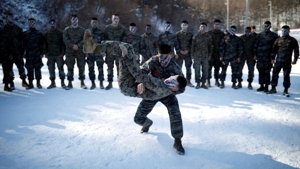Zwei Soldaten mit Gesichtsbemalung üben Nahkampf vor einer Gruppe von Soldaten im Schnee.