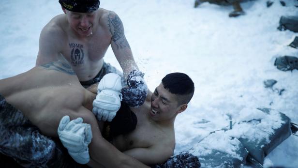Drei Männer raufen unbekleidet und mit Handschuhen im Schnee.