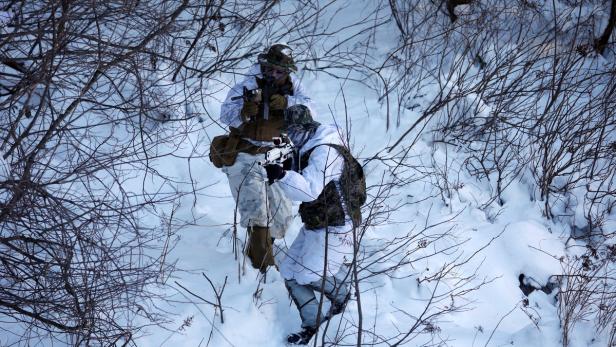 Zwei Soldaten in Wintertarnkleidung stehen mit Gewehren im Schnee.