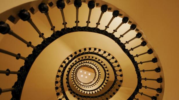 Blick von unten auf eine Wendeltreppe mit dunklem Geländer.
