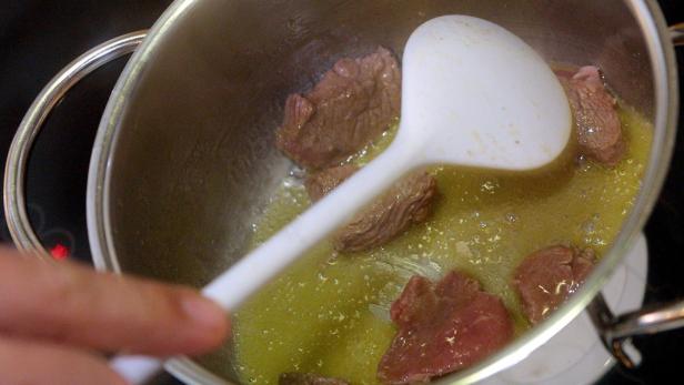 Fleischstücke werden in einem Topf mit einer Schöpfkelle umgerührt.