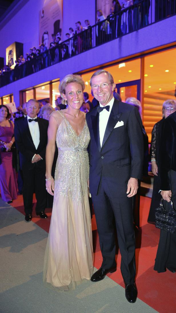 Ein Mann im Smoking und eine Frau im Abendkleid posieren auf einem roten Teppich.