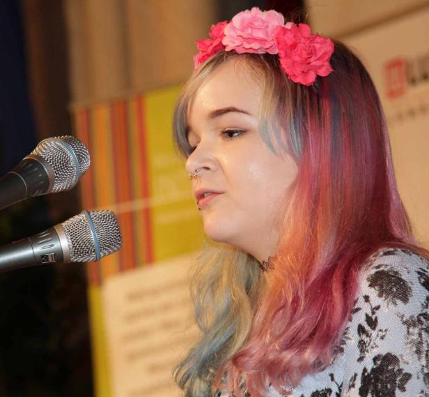 Eine junge Frau mit Blumenkranz singt vor zwei Mikrofonen.