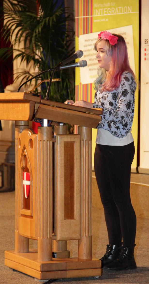 Eine junge Frau mit Blumenkranz hält eine Rede an einem Rednerpult.