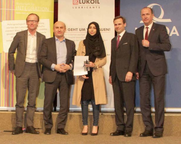 Fünf Personen posieren auf einer Bühne vor Logos von Lukoil und Wirtschaft für Integration.