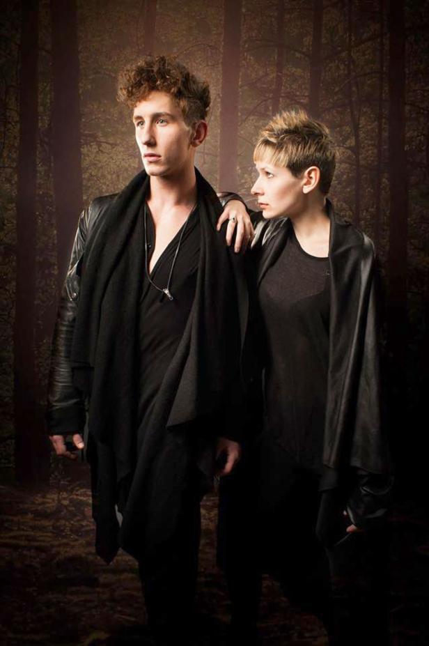 Ein Mann und eine Frau posieren vor einem dunklen Waldhintergrund.