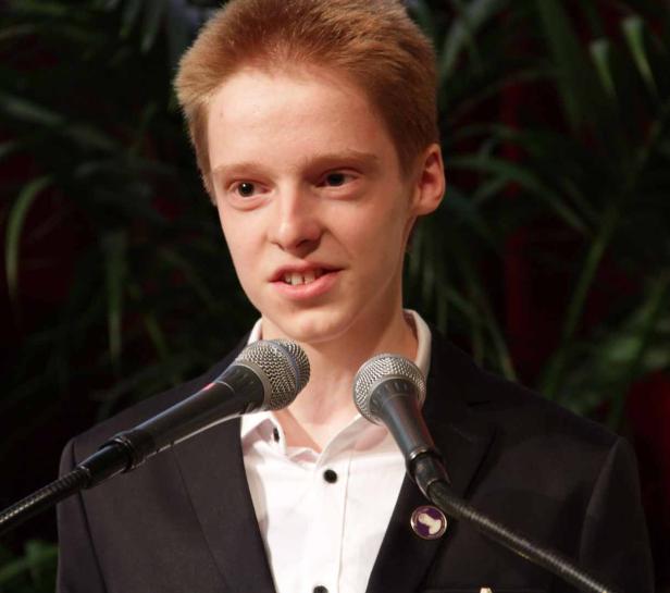 Ein junger Mann mit roten Haaren spricht vor zwei Mikrofonen.