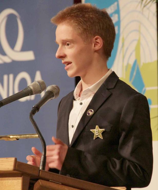 Ein junger Mann hält eine Rede an einem Rednerpult mit Mikrofonen.