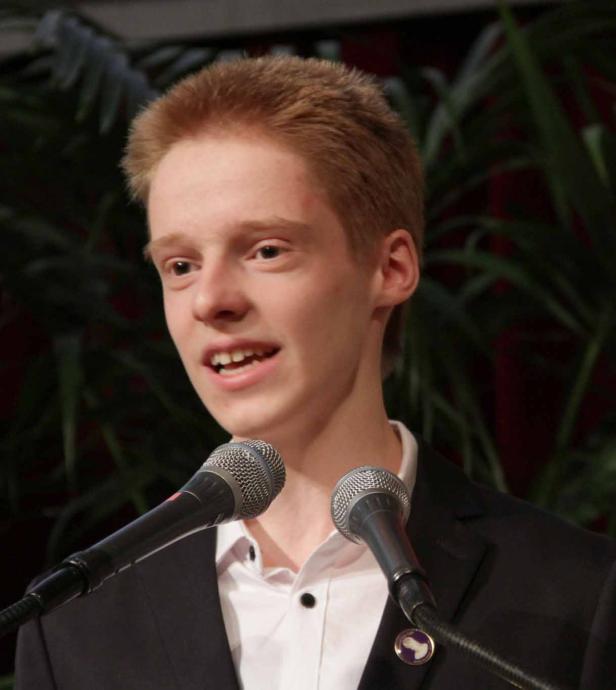 Ein junger Mann mit roten Haaren spricht vor zwei Mikrofonen.