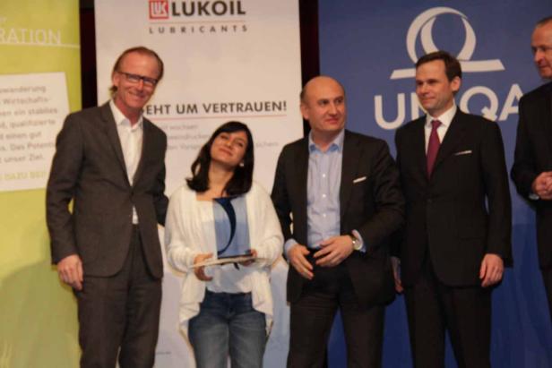 Eine Frau hält eine Auszeichnung auf einer Bühne mit mehreren Männern im Anzug.