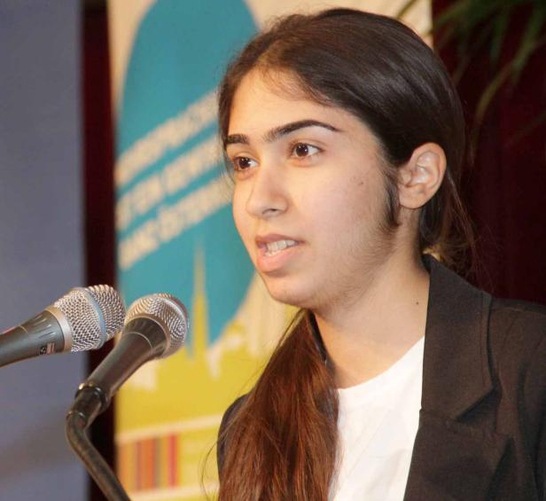 Eine junge Frau spricht bei einer Veranstaltung vor zwei Mikrofonen.