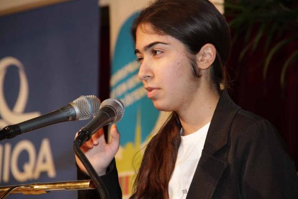 Eine junge Frau spricht bei einer Veranstaltung vor zwei Mikrofonen.