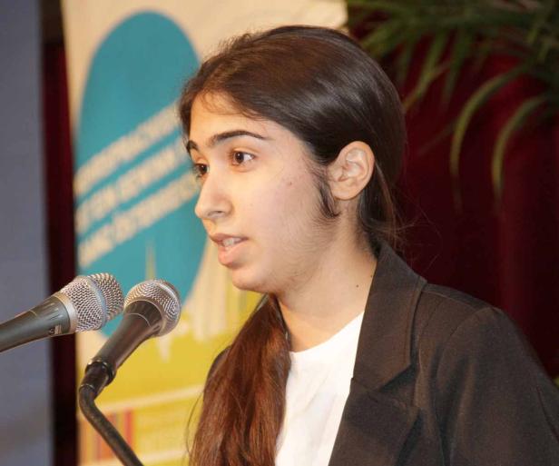 Eine junge Frau spricht bei einer Veranstaltung vor zwei Mikrofonen.