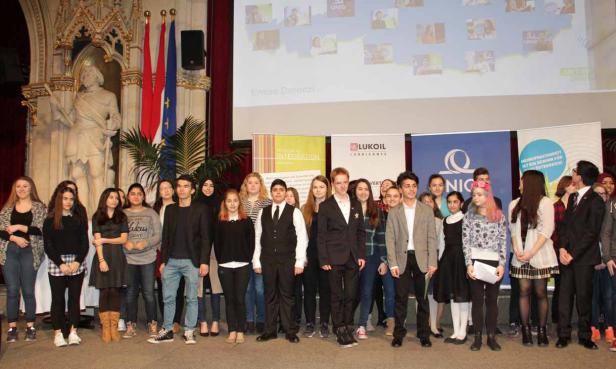 Eine Gruppe junger Leute steht vor Flaggen und Werbebannern in einem festlichen Saal.