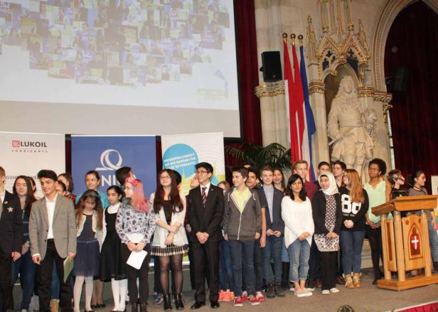 Eine Gruppe von Jugendlichen steht auf einer Bühne vor Bannern und Flaggen.