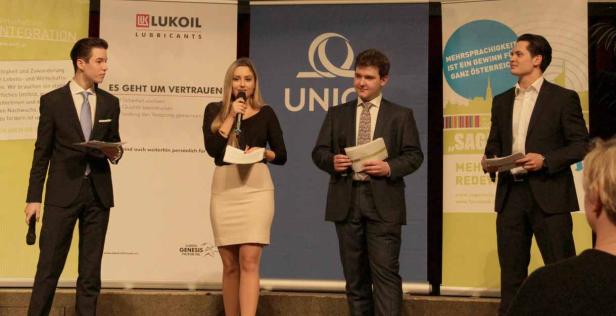 Vier Personen stehen auf einer Bühne vor Bannern und halten Reden.