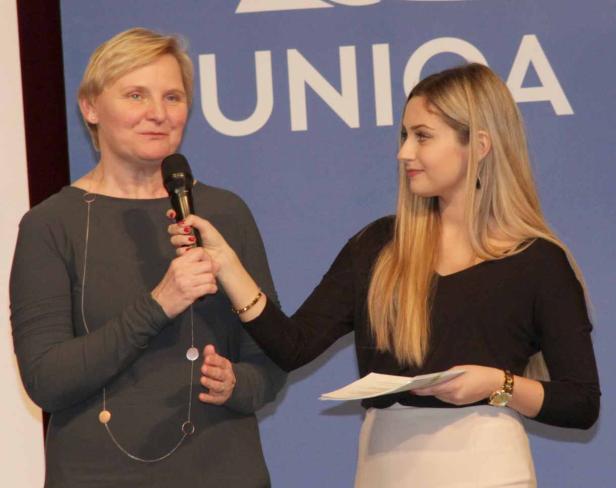 Eine Frau hält ein Mikrofon, während eine andere Frau ihr ein Blatt Papier reicht.