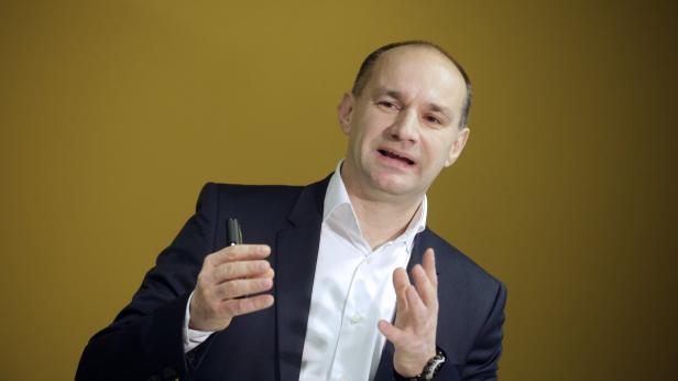 Ein Mann im Anzug gestikuliert vor einem gelben Hintergrund.