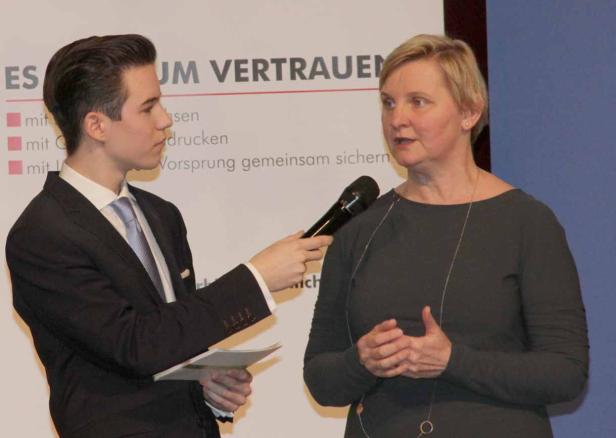 Ein junger Mann interviewt eine Frau mit einem Mikrofon vor einem Banner.