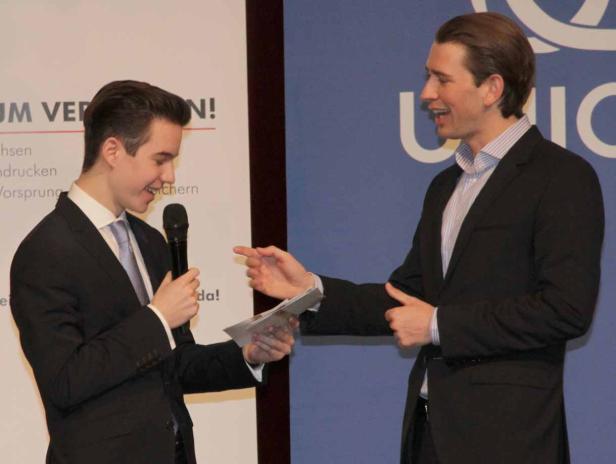 Zwei Männer in Anzügen unterhalten sich auf einer Veranstaltung.