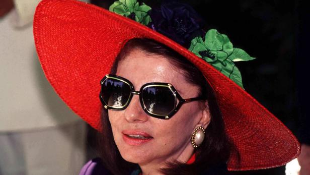Eine Frau mit Sonnenbrille und einem roten Hut mit Blumenapplikationen.