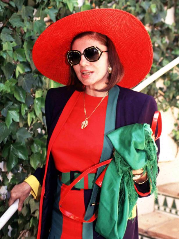 Eine Frau mit Sonnenbrille und rotem Hut steht vor einer grünen Wand.