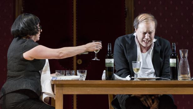 Eine Frau reicht einem Mann am Tisch ein Glas Wein.