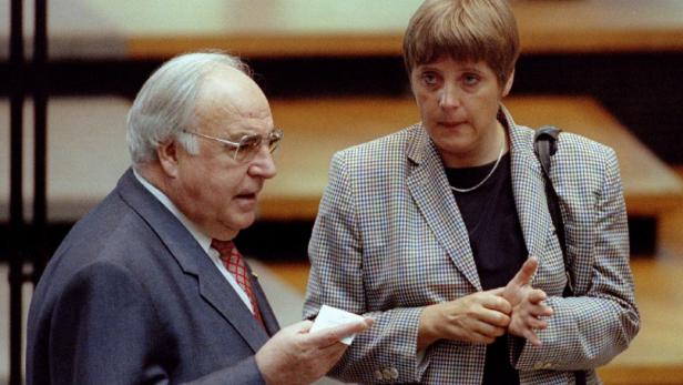 Helmut Kohl spricht mit Angela Merkel, die eine karierte Jacke trägt.