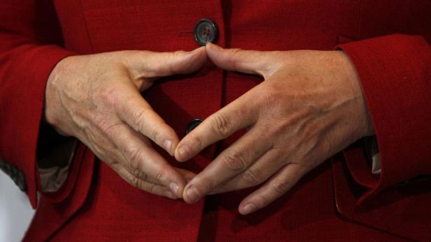 Die Hände einer Person liegen vor einem roten Blazer mit zwei Knöpfen.